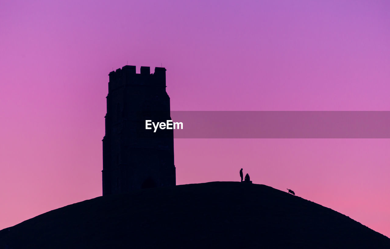 Silhouette tower church and  person standing by pink against sky during sunset