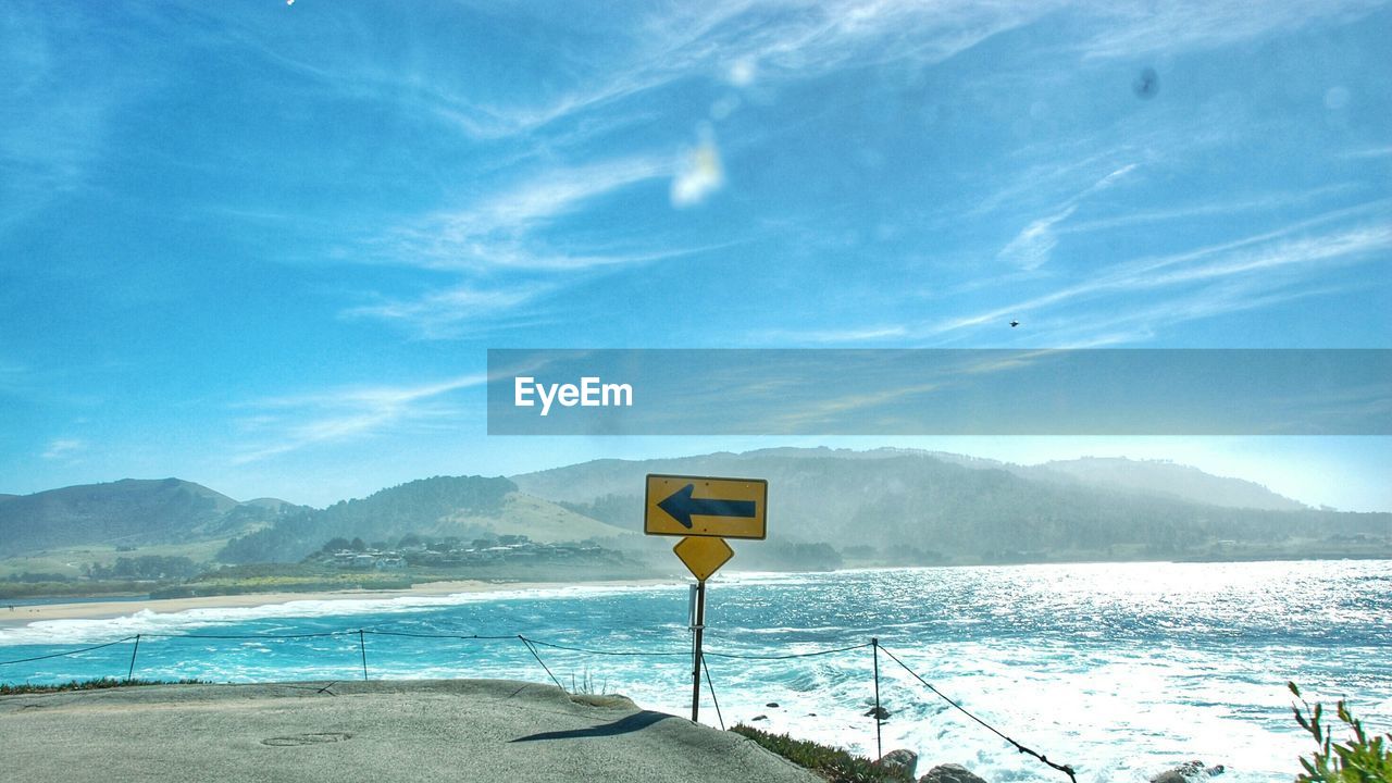 Sign on road by sea against sky