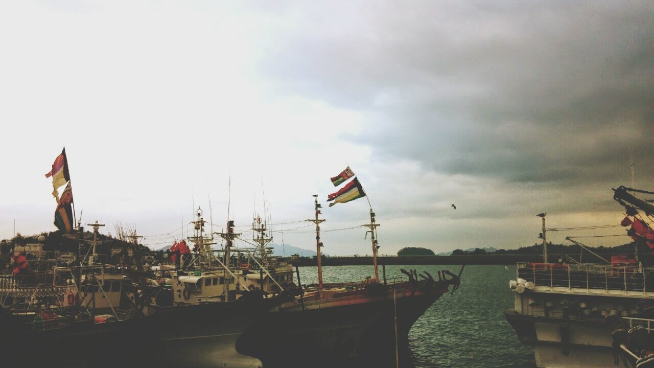 BOATS ON HARBOR AGAINST CLOUDY SKY