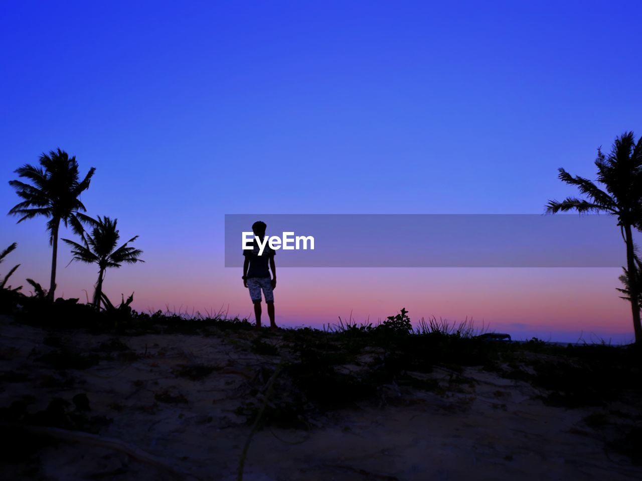 SILHOUETTE MAN STANDING ON STREET DURING SUNSET