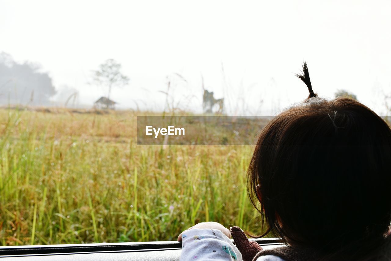 Rear view of boy by window against sky
