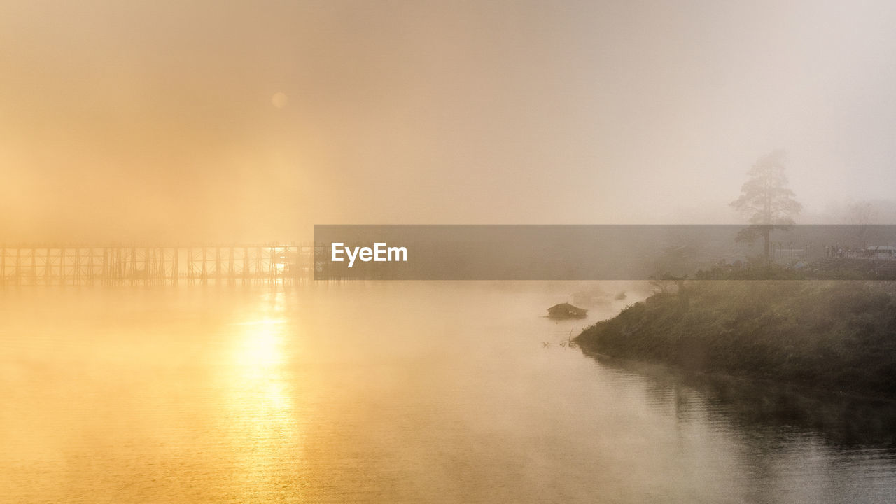 Footbridge over river in foggy weather during sunrise
