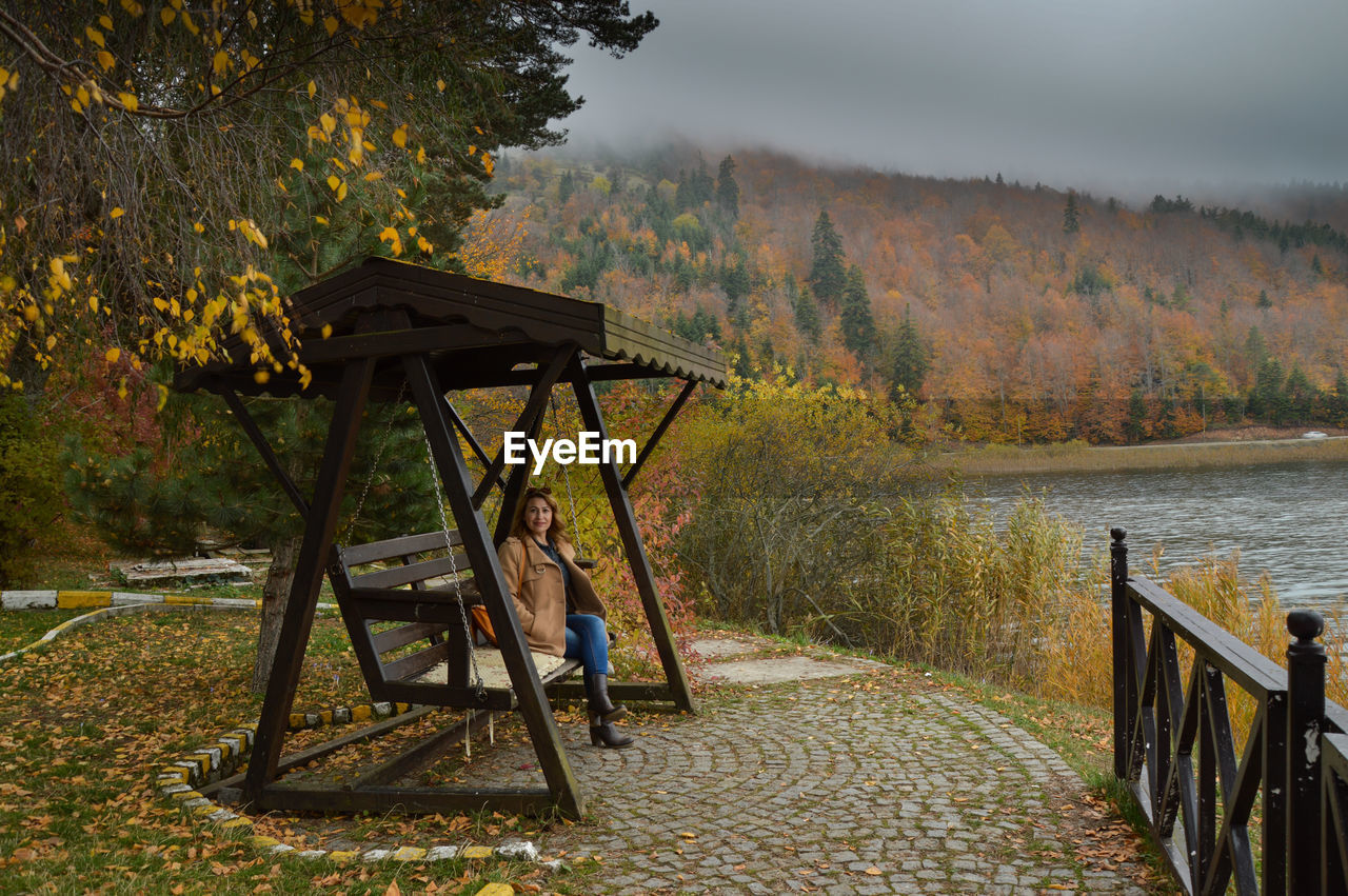 Portrait of woman sitting on wooden swing by river