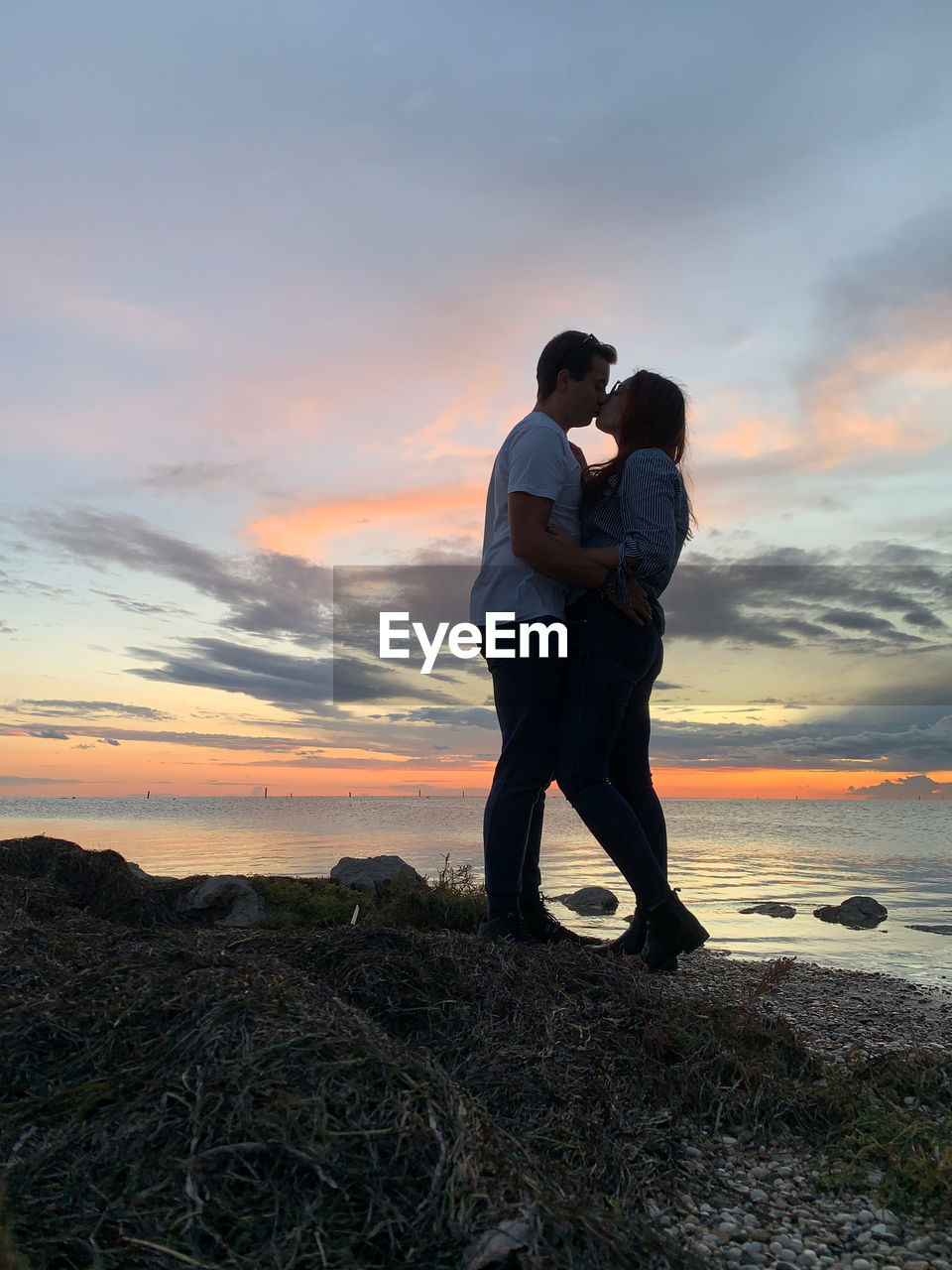 Friends standing on shore against sky during sunset