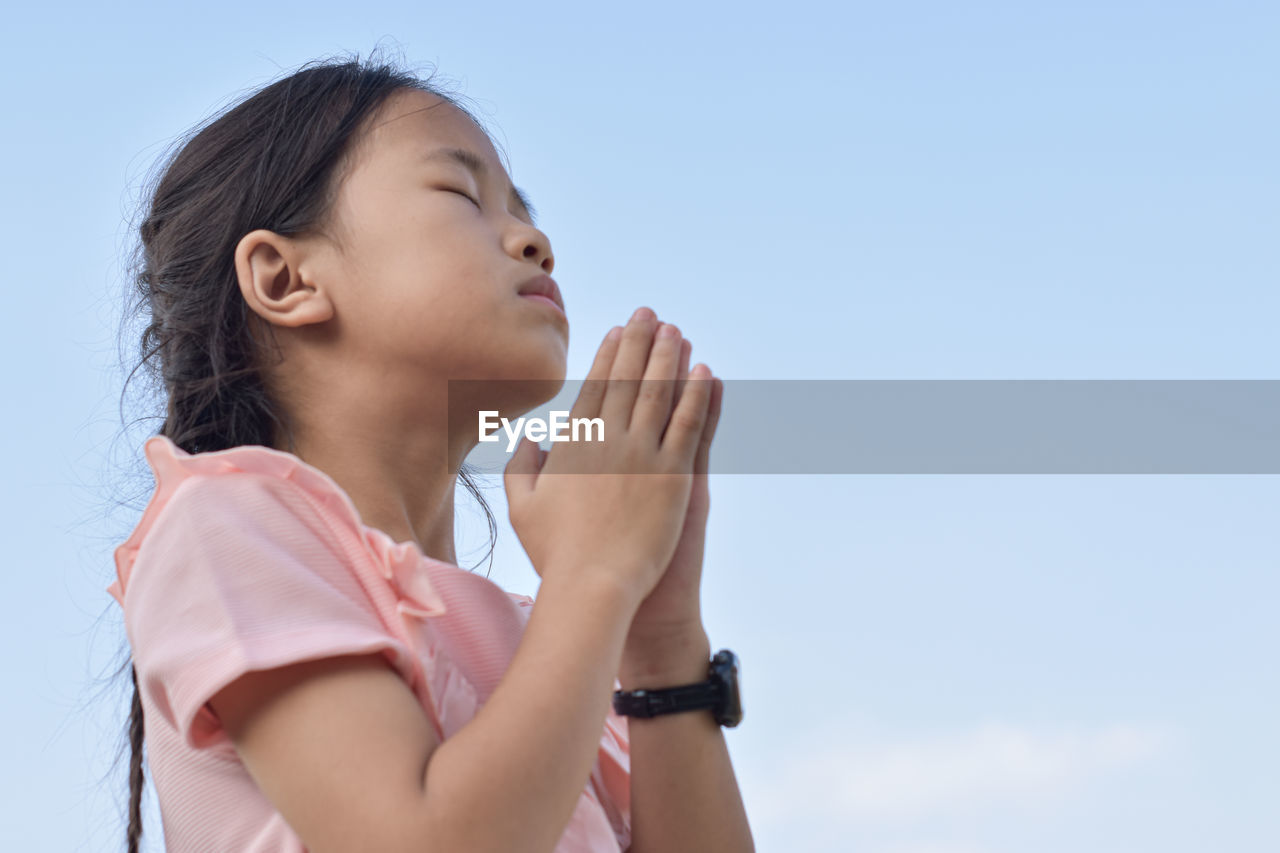 Close up of child girl hands in prayer with hope faith over blue sky background.