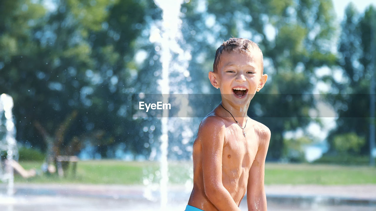 Excited boy of seven years having fun between water jets, in fountain, run around, sprinkle, have