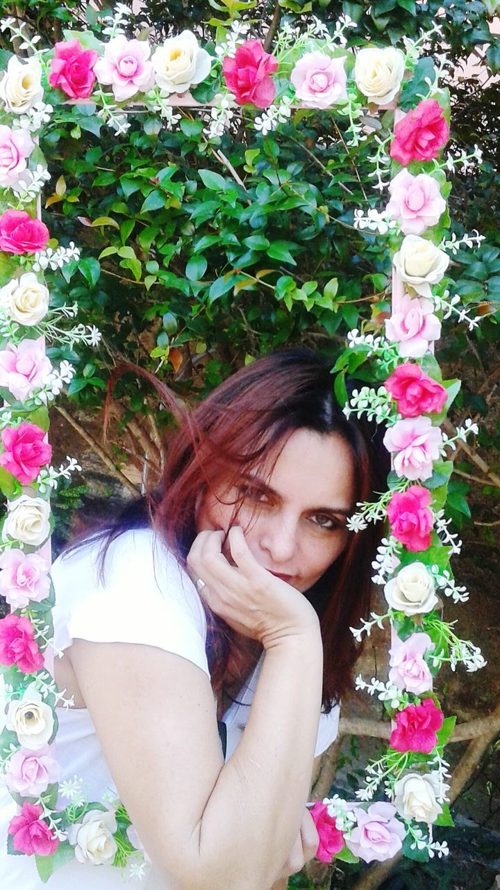 Portrait of woman with hand on chin looking through flower frame