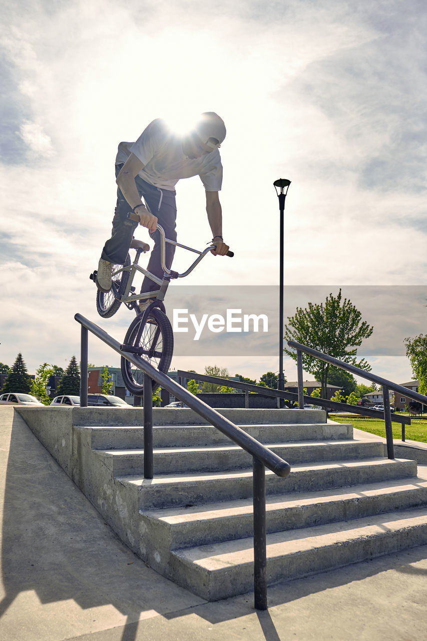 Male rider riding bmx bike on railing against sky at skateboard park during sunny day