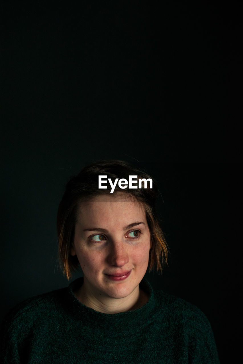 Beautiful woman looking away against black background