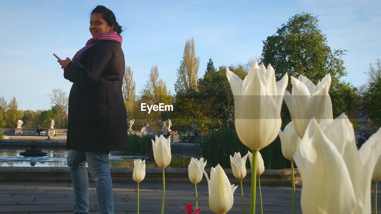 Portrait of pregnant woman standing by white tulips in park