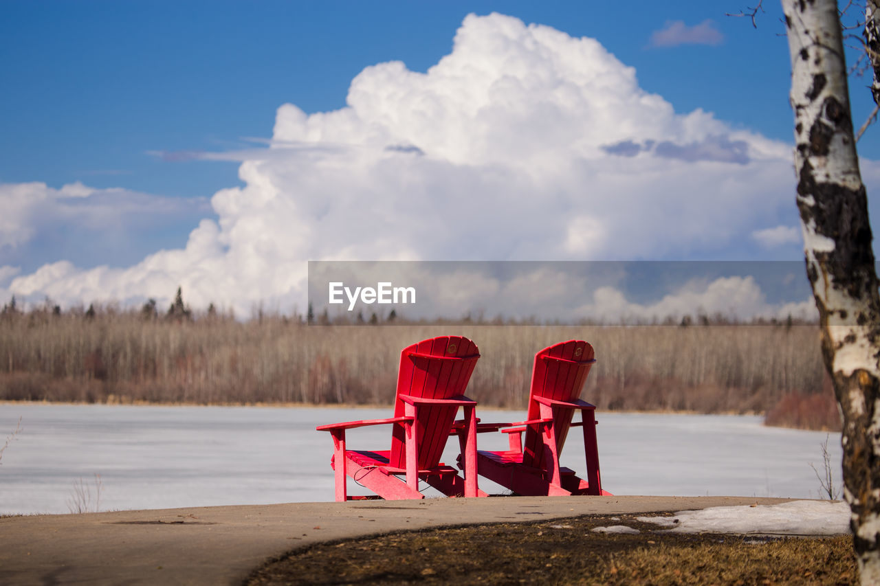 Red chair by lake against sky
