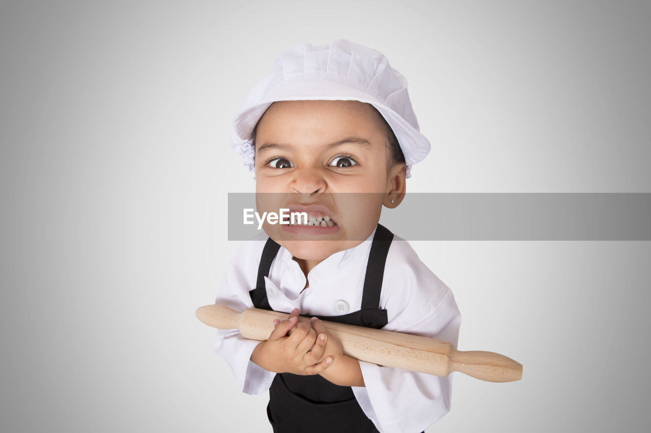 Portrait of girl in chef uniform holding rolling pin while standing against purple background