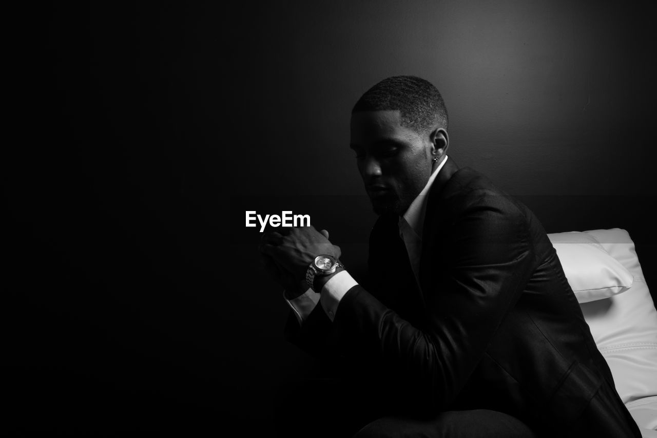 Thoughtful man wearing suit sitting on bed against wall