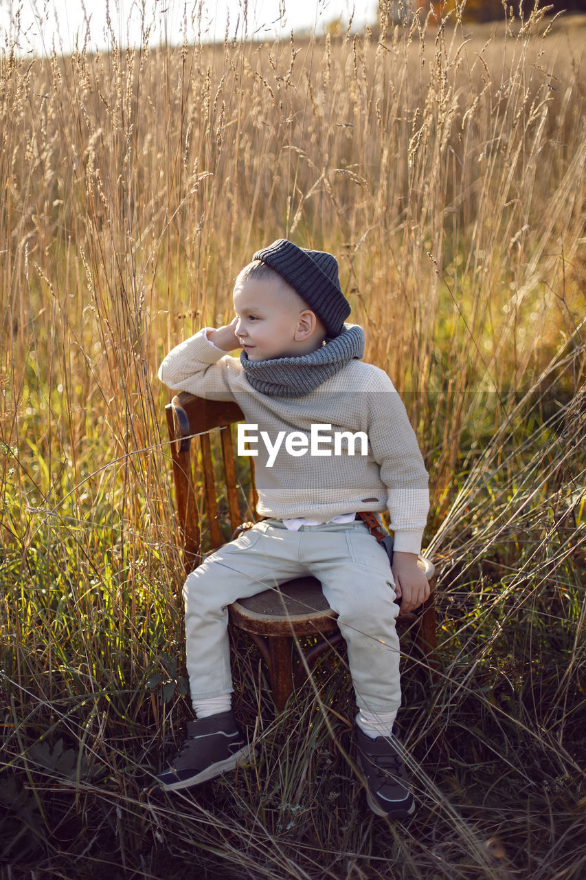 Fashionable boy child sitting on a chair in autumn on the field