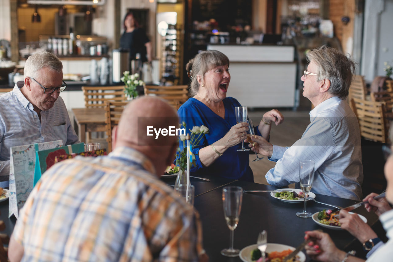 Senior couple toasting flutes while having lunch with friends in restaurant