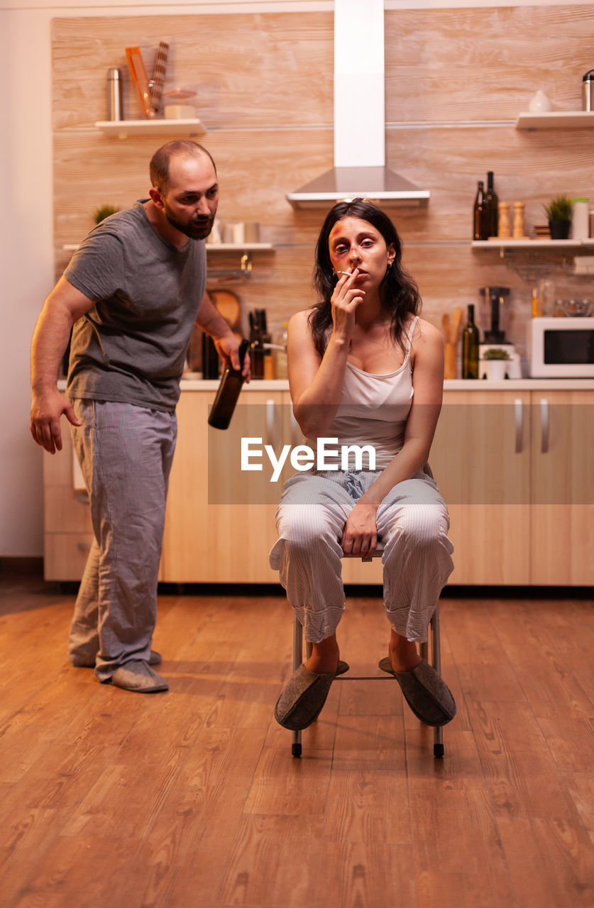 portrait of young woman using mobile phone while sitting on hardwood floor