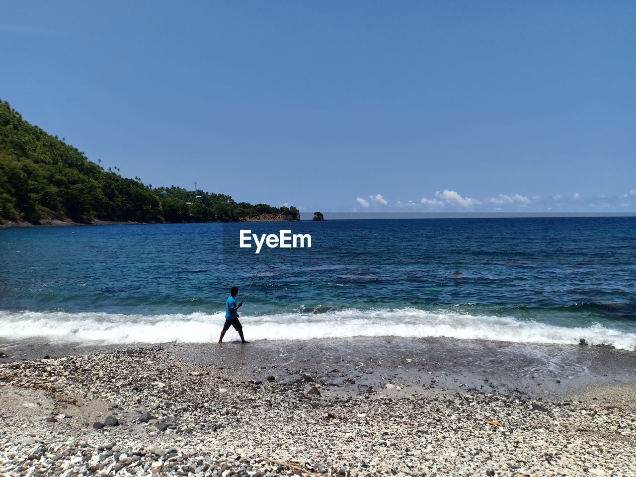 Side view of man fishing at beach against sky