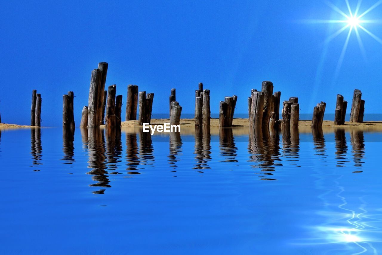 WOODEN POSTS IN SEA AGAINST CLEAR SKY