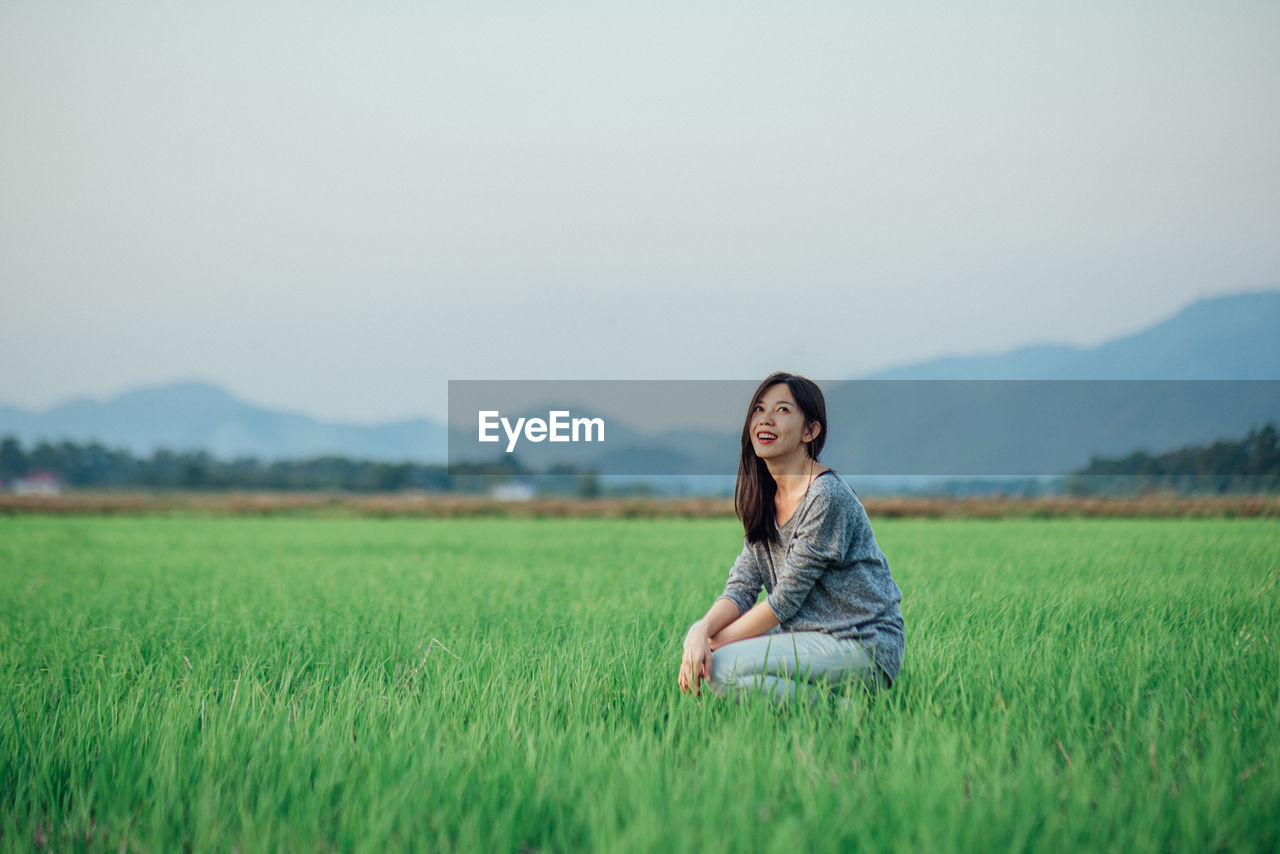 Smiling woman crouching on field against sky