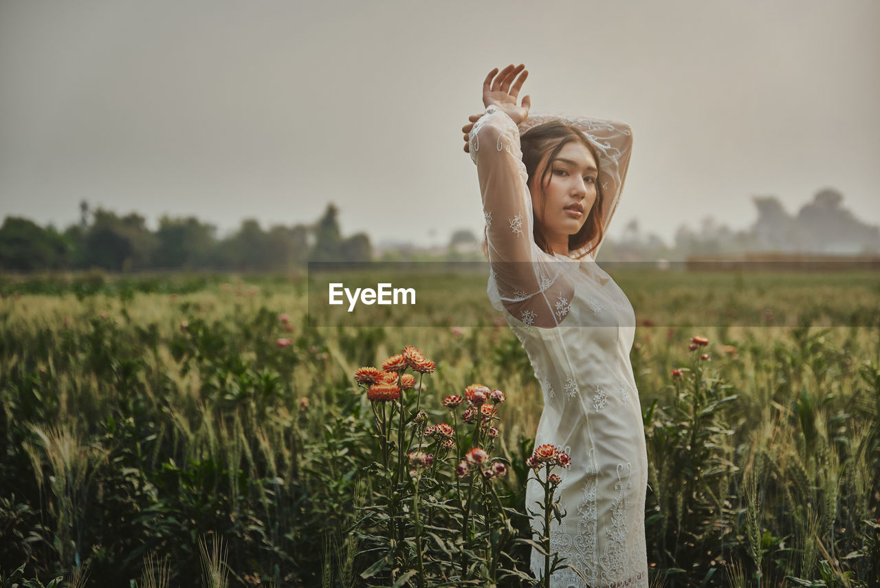 Portrait of girl standing by flowering plants against sky