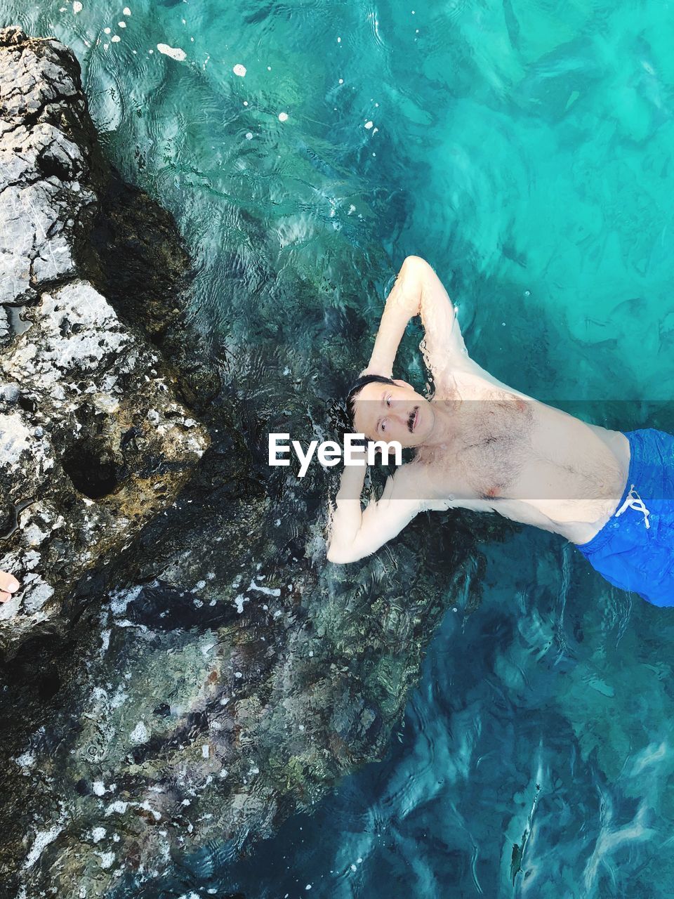 High angle view of shirtless man lying in sea