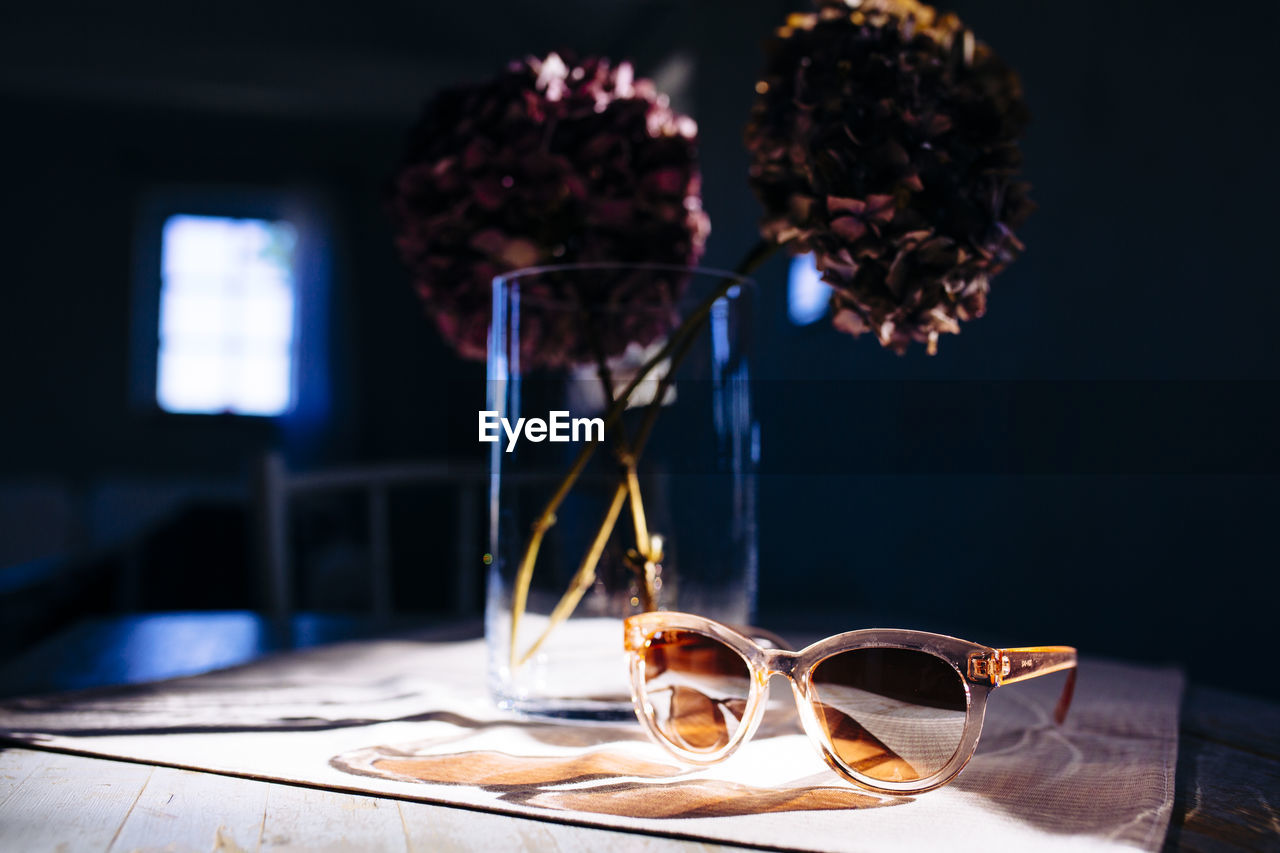 Close-up of flower vase and sunglasses on table.