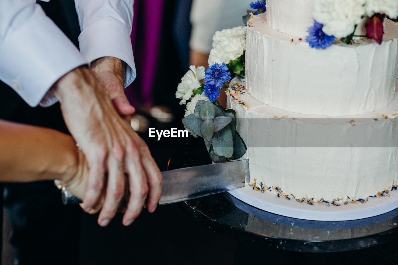 Cropped hands of couple cutting wedding cake