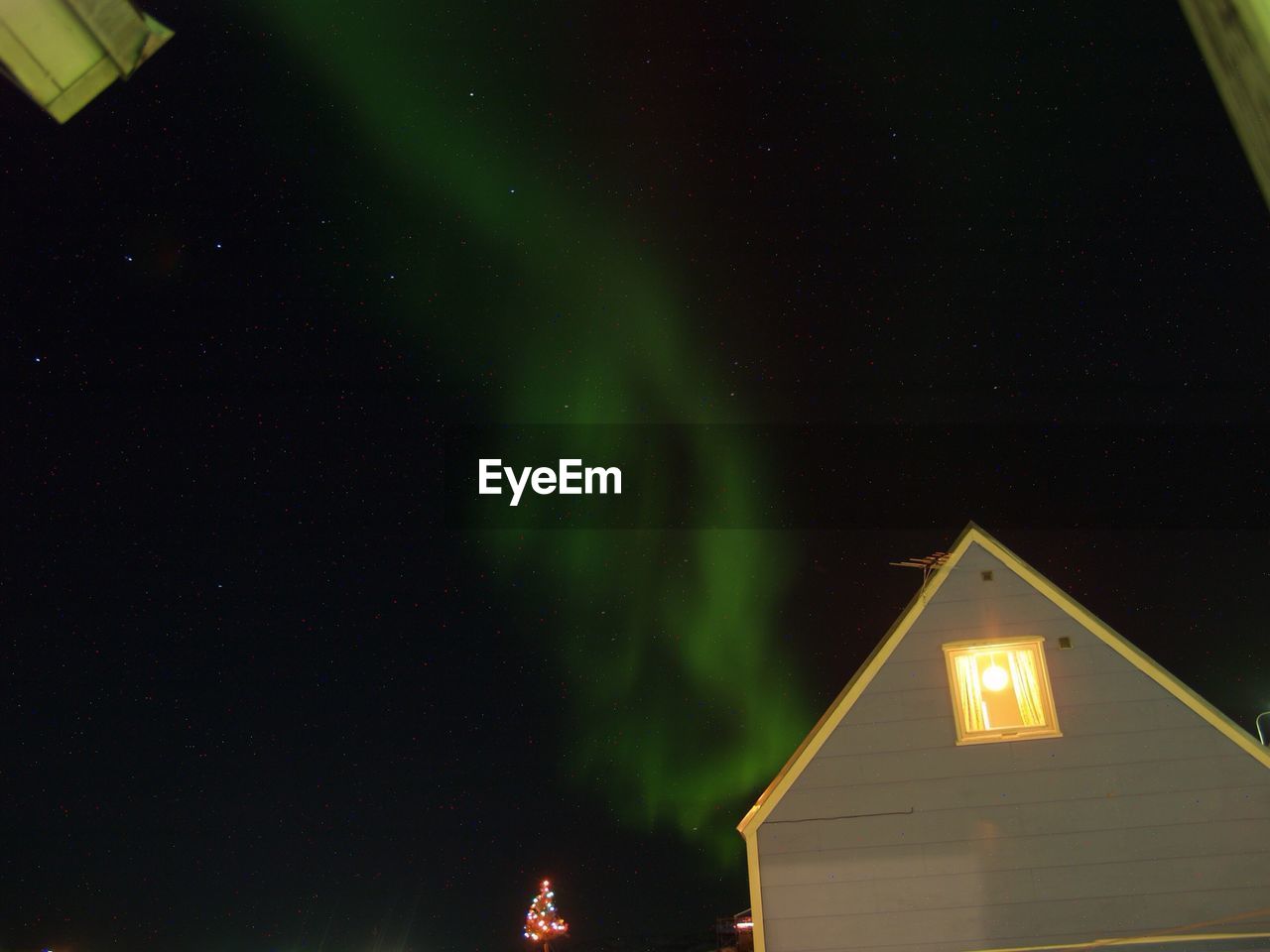 Low angle view of illuminated house against aurora in sky at night