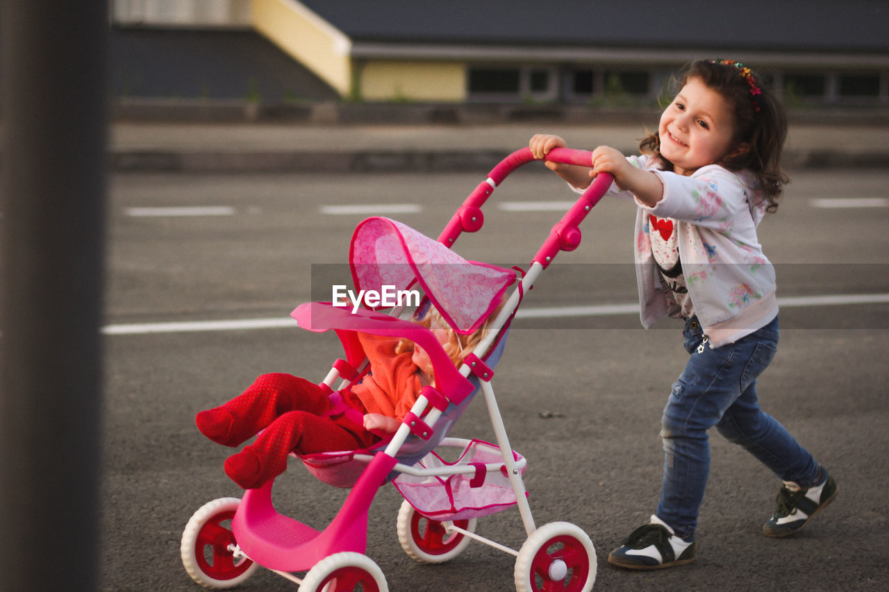 Cute girl with doll in baby stroller walking on roads