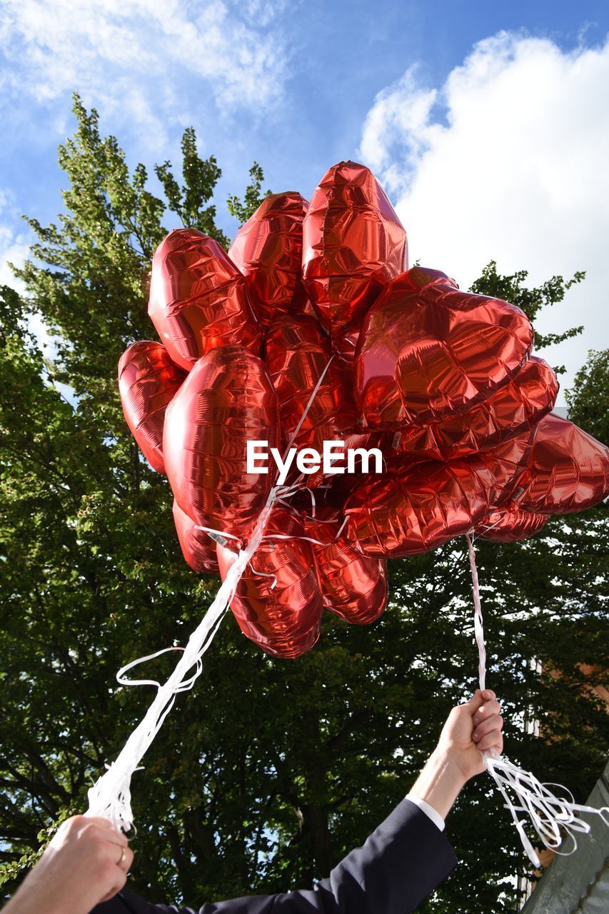 Low angle view of hand holding balloons against sky