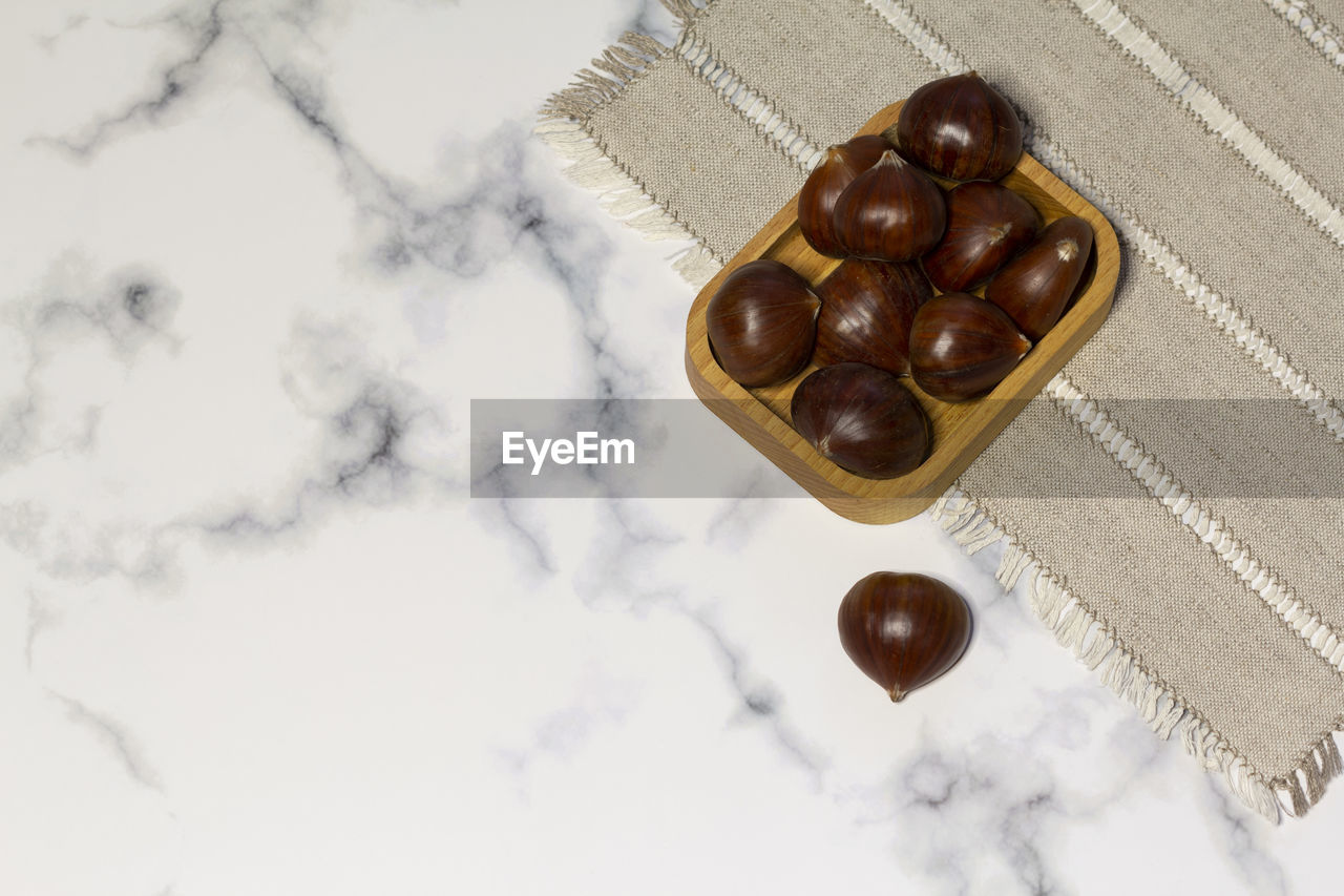 Edible chestnuts in a wooden plate, white marble background, linen napkin