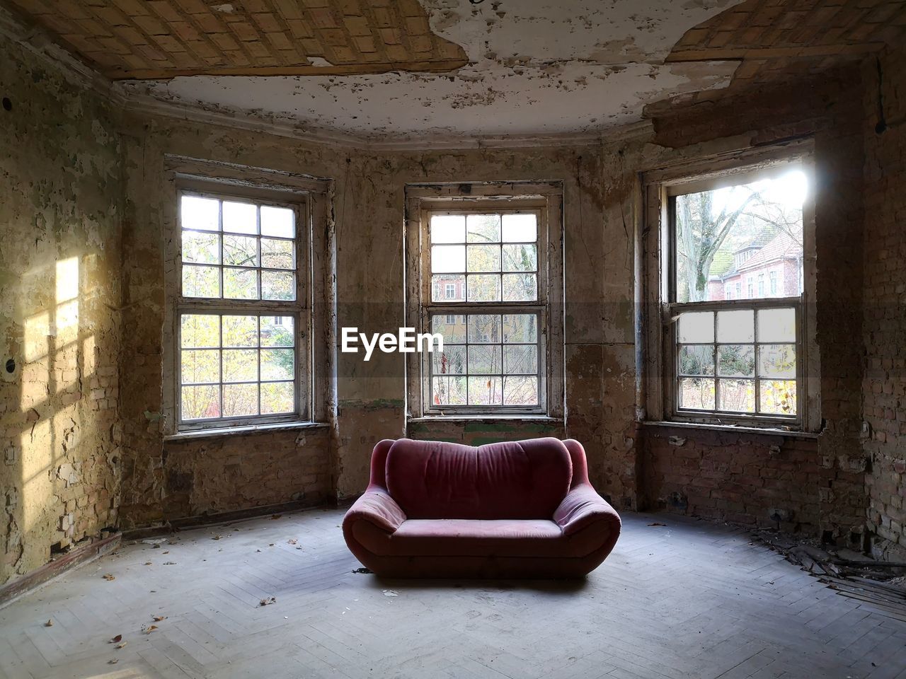 Interior of abandoned house with bis windows, light reflection on a wall and a sofa