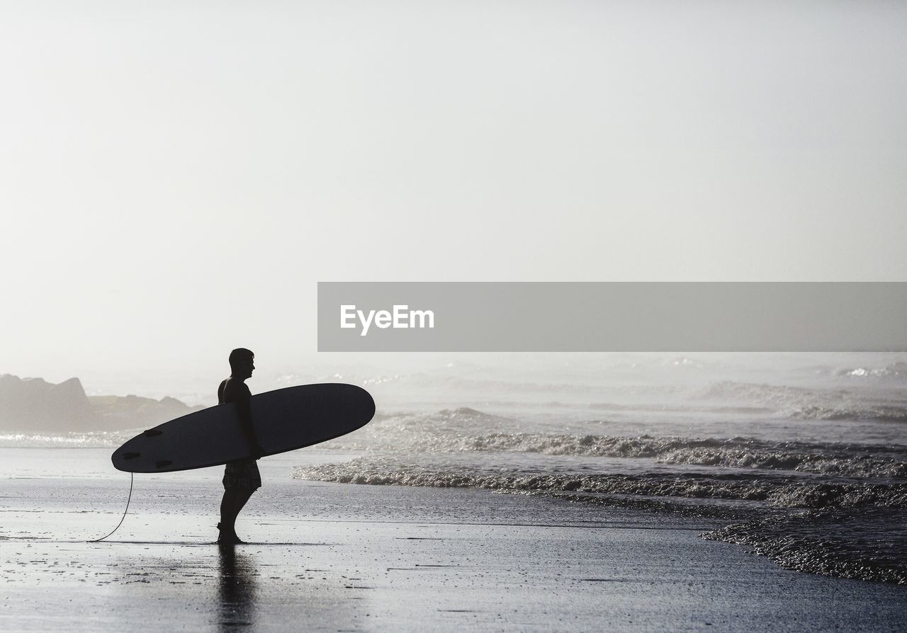 Surfer holding surfboard while standing on shore at beach