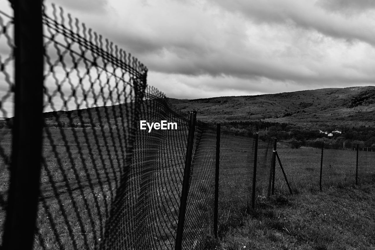 FENCE ON FIELD AGAINST SKY SEEN THROUGH CHAINLINK