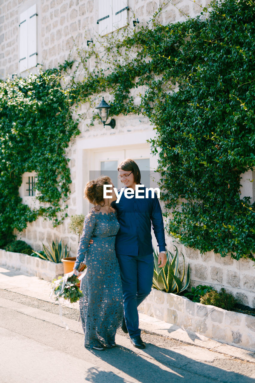 REAR VIEW OF COUPLE STANDING BY PLANTS