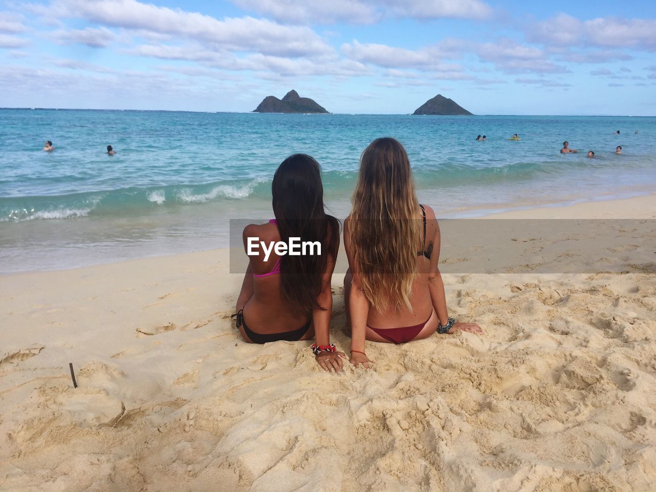 Rear view of female friends sitting on sand at beach against sky