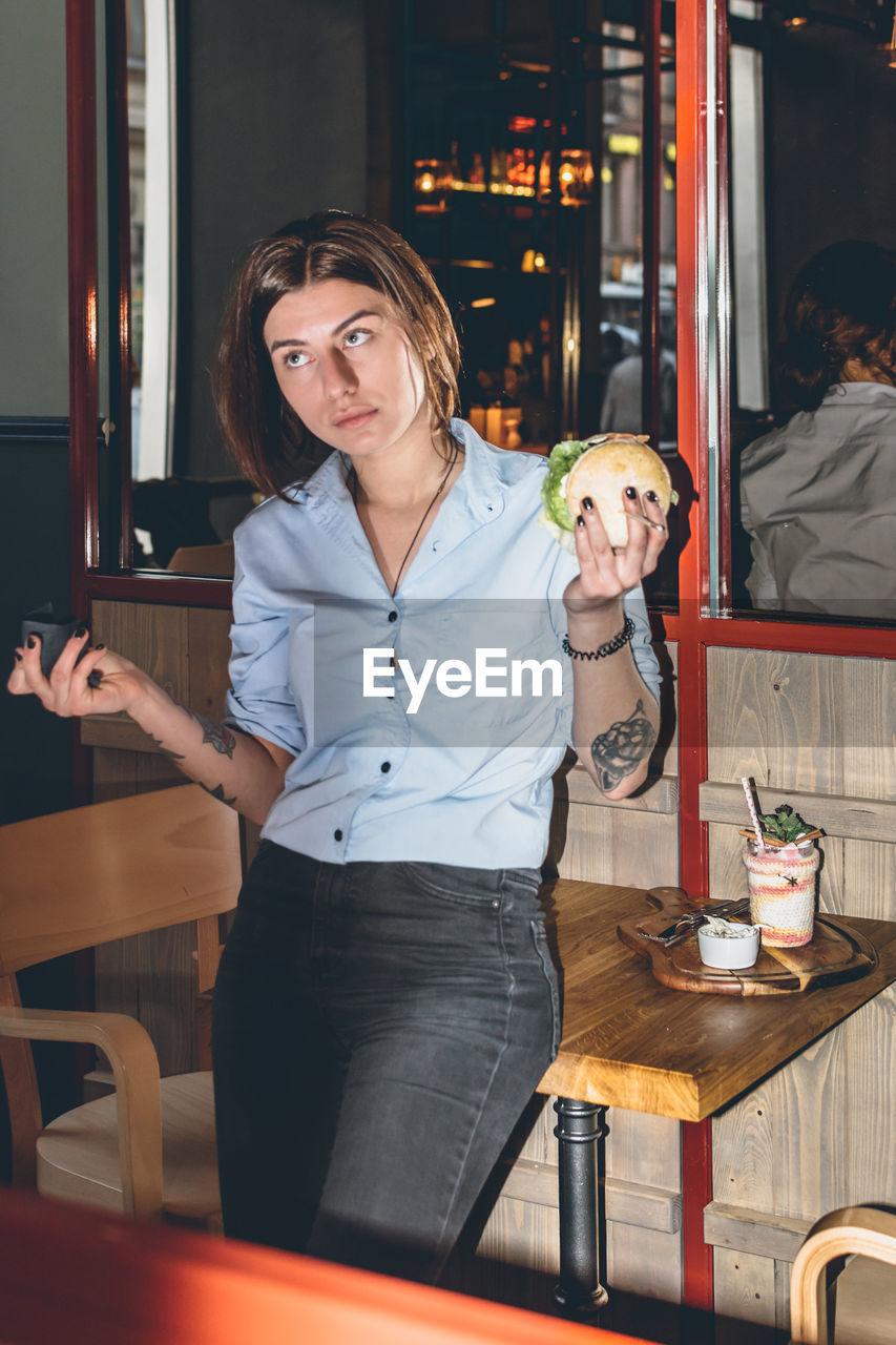 Woman holding burger standing at restaurant