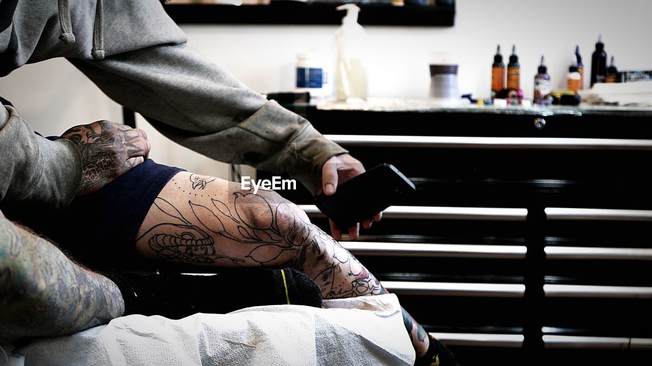Customer with tattoo holding mobile phone by artist at studio
