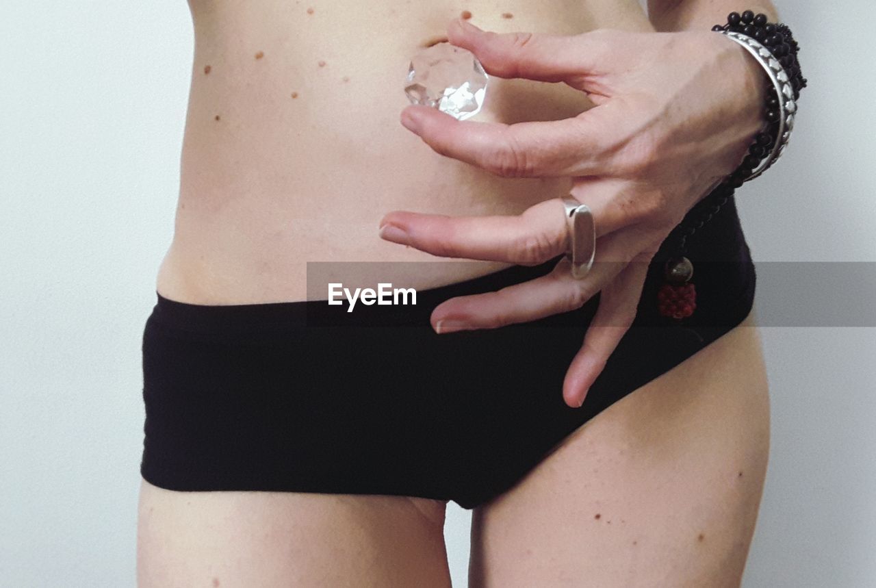 Midsection of woman holding diamond standing against white background