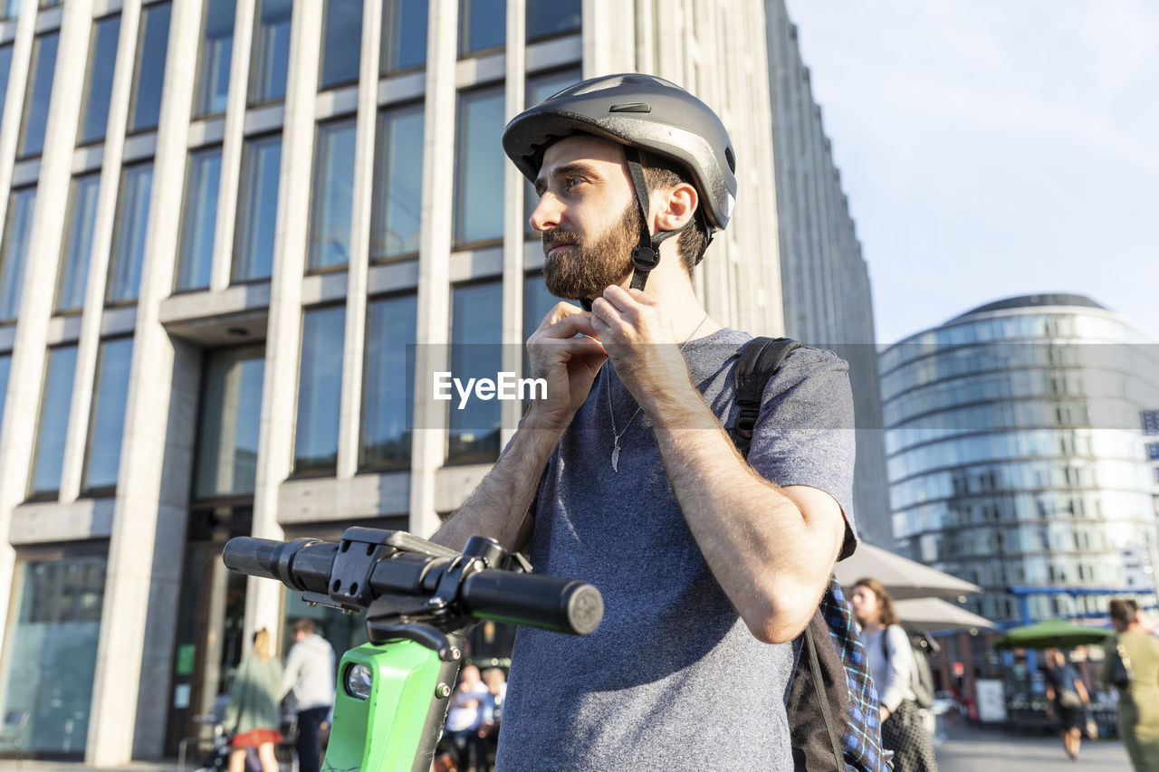 Man using e-scooter in berlin, fastening safety helmet, germany