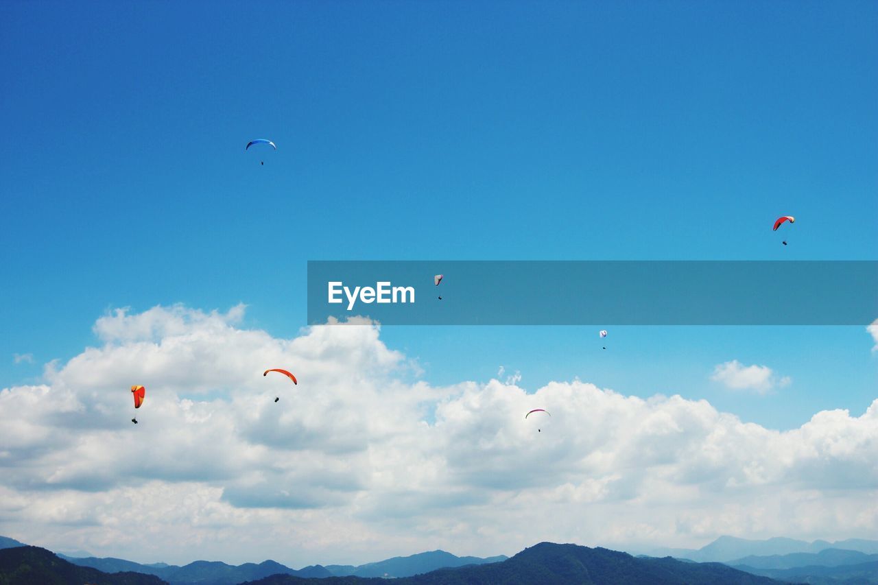 People paragliding over mountain against cloudy sky
