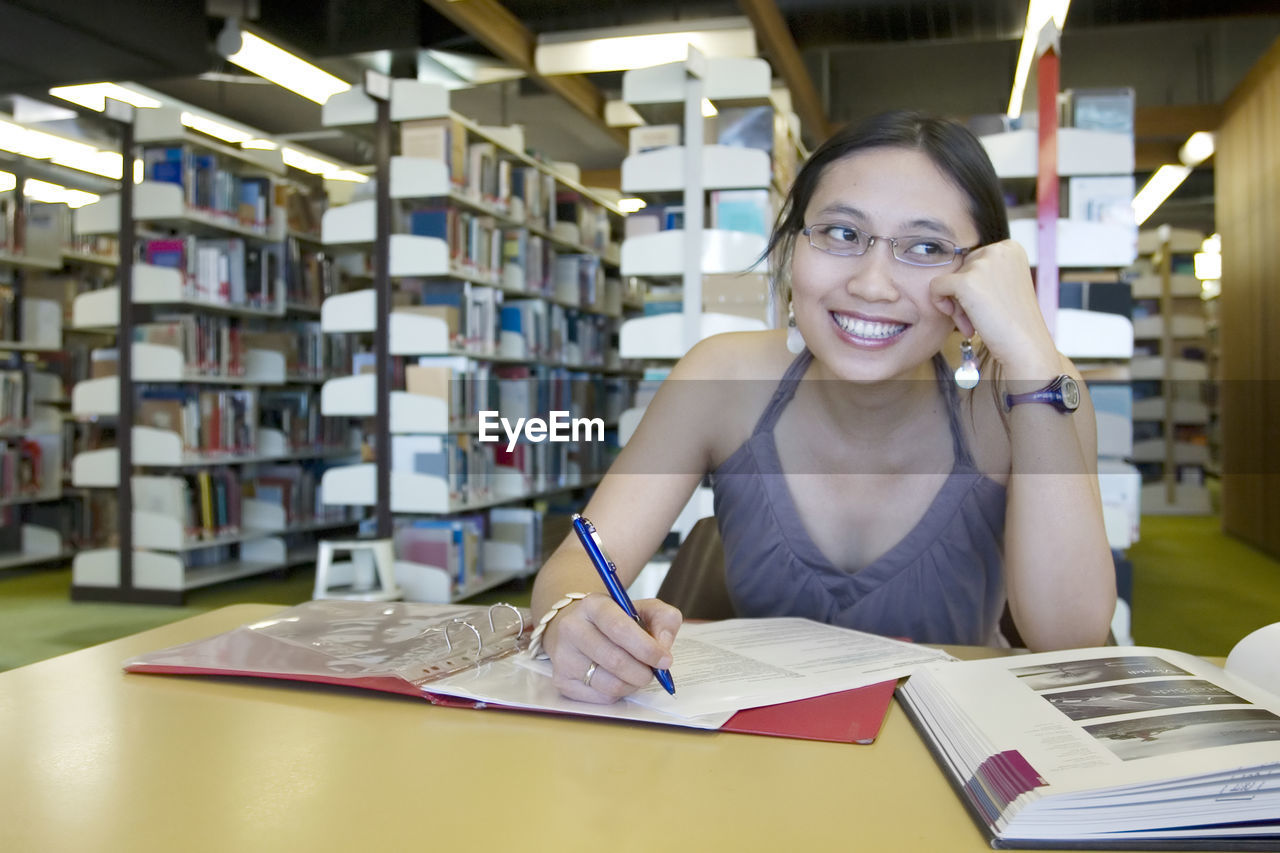 Woman writing in book while sitting at library