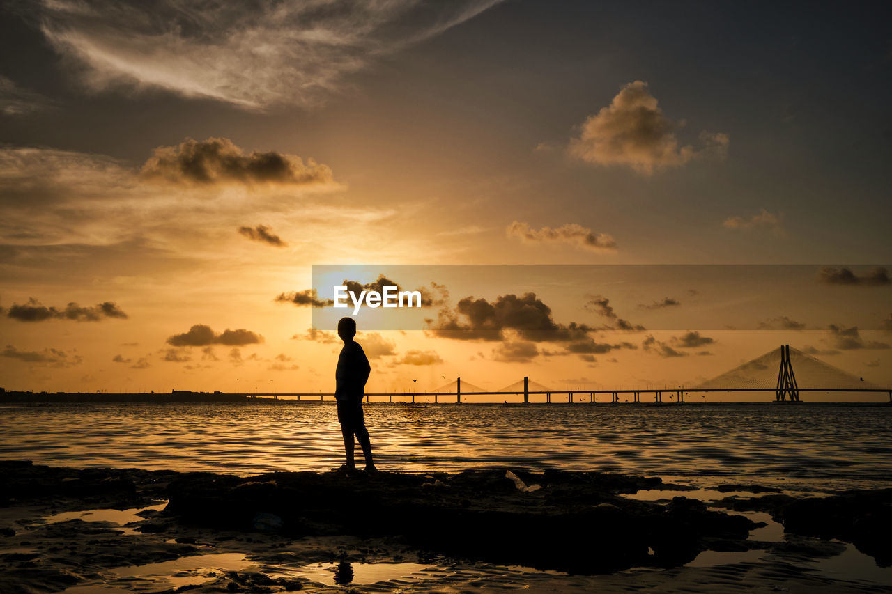 SILHOUETTE MAN STANDING AT BEACH DURING SUNSET