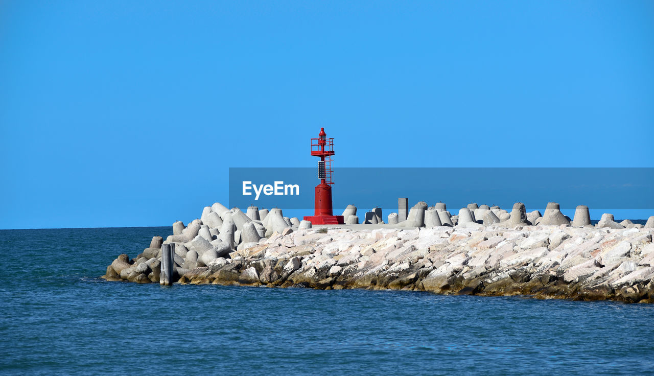 lighthouse, tower, guidance, water, sea, breakwater, sky, architecture, security, protection, built structure, blue, ocean, coast, building, nature, building exterior, clear sky, rock, beach, shore, no people, day, scenics - nature, coastline, land, horizon over water, groyne, copy space, outdoors, horizon, beauty in nature, non-urban scene, travel destinations, wave, animal themes, travel, bay, animal