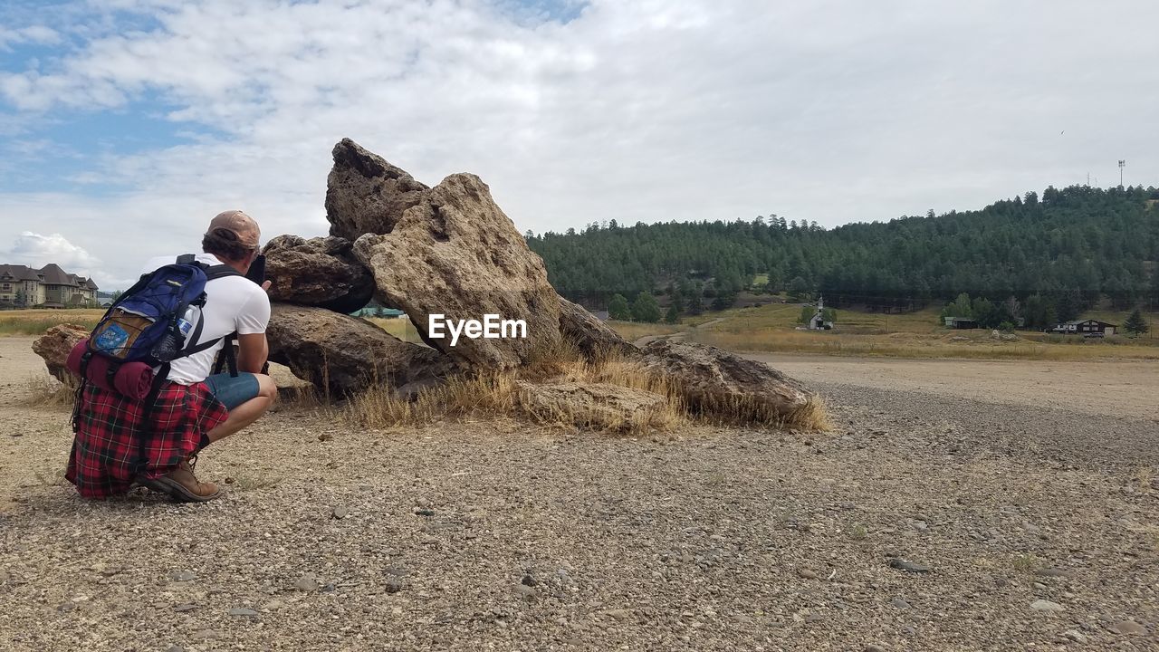 sky, nature, adult, cloud, full length, land, men, landscape, day, leisure activity, geology, one person, travel, outdoors, environment, activity, rural scene, plant, tree, sitting, scenics - nature, sand, occupation, rock, non-urban scene, rear view, travel destinations, lifestyles, clothing, mountain, backpack