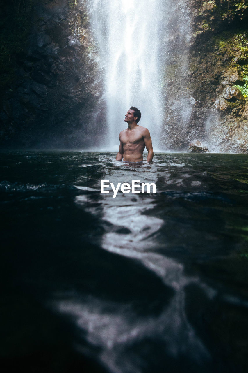 Rear view of man in water infront of waterfall.