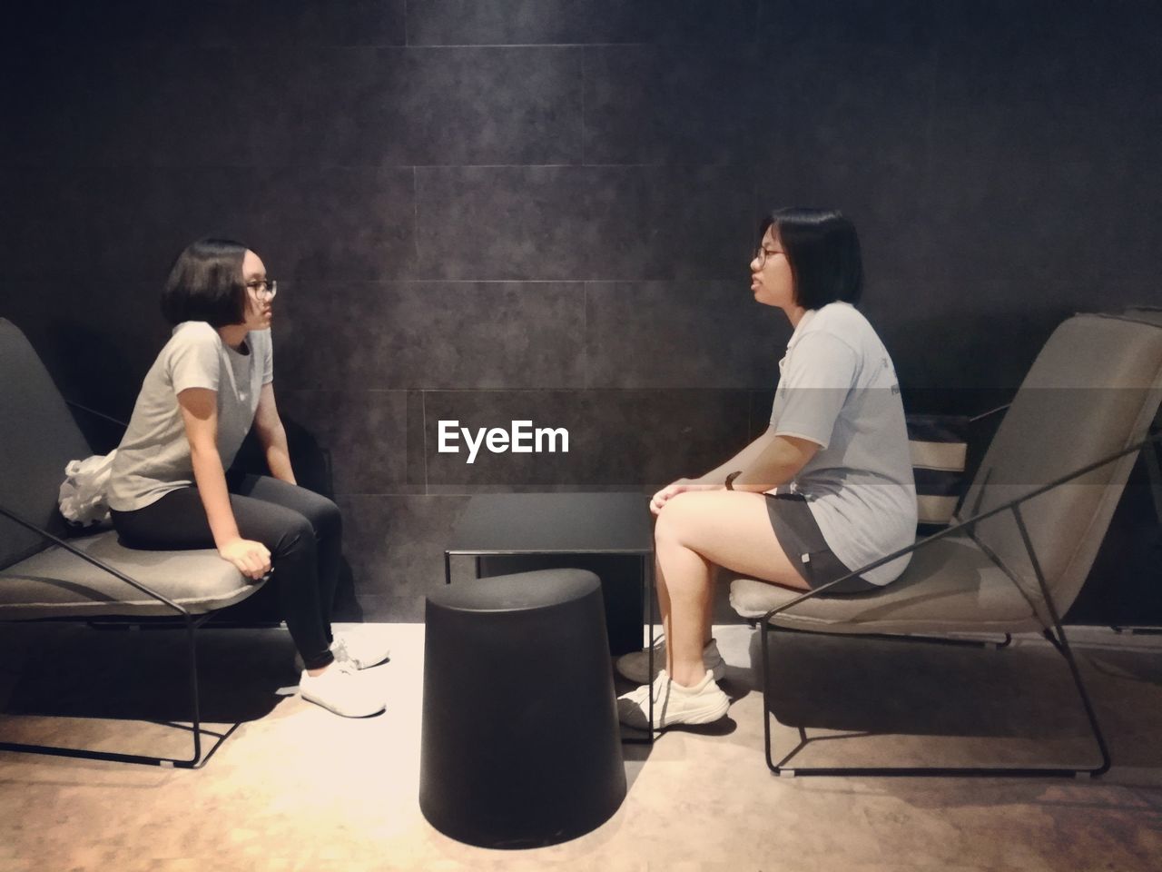 SIDE VIEW OF YOUNG COUPLE SITTING ON CHAIR IN ROOM