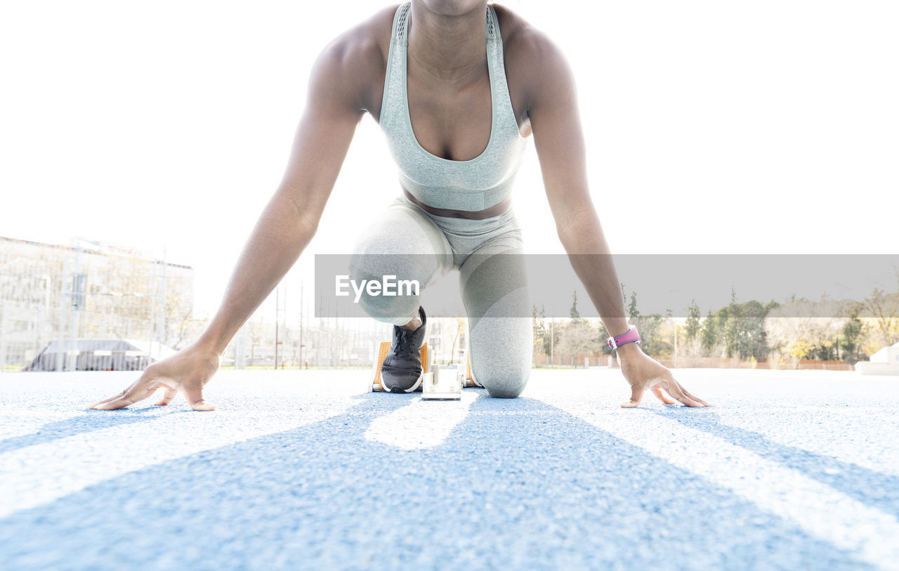 From below of african american female runner in starting blocks sitting in crouch position while getting ready for sprint at stadium during workout