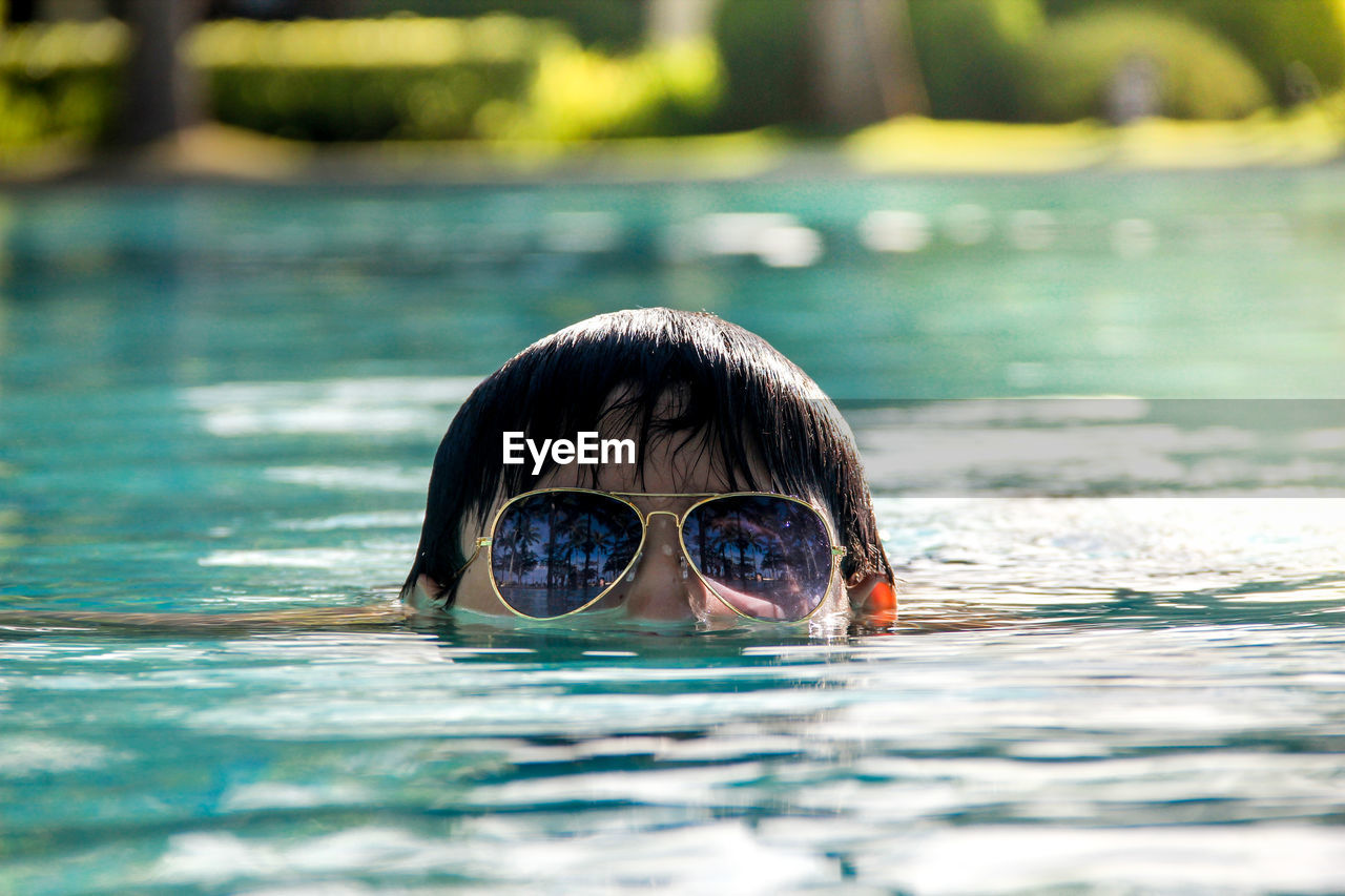 High section of person wearing sunglasses while swimming in lake