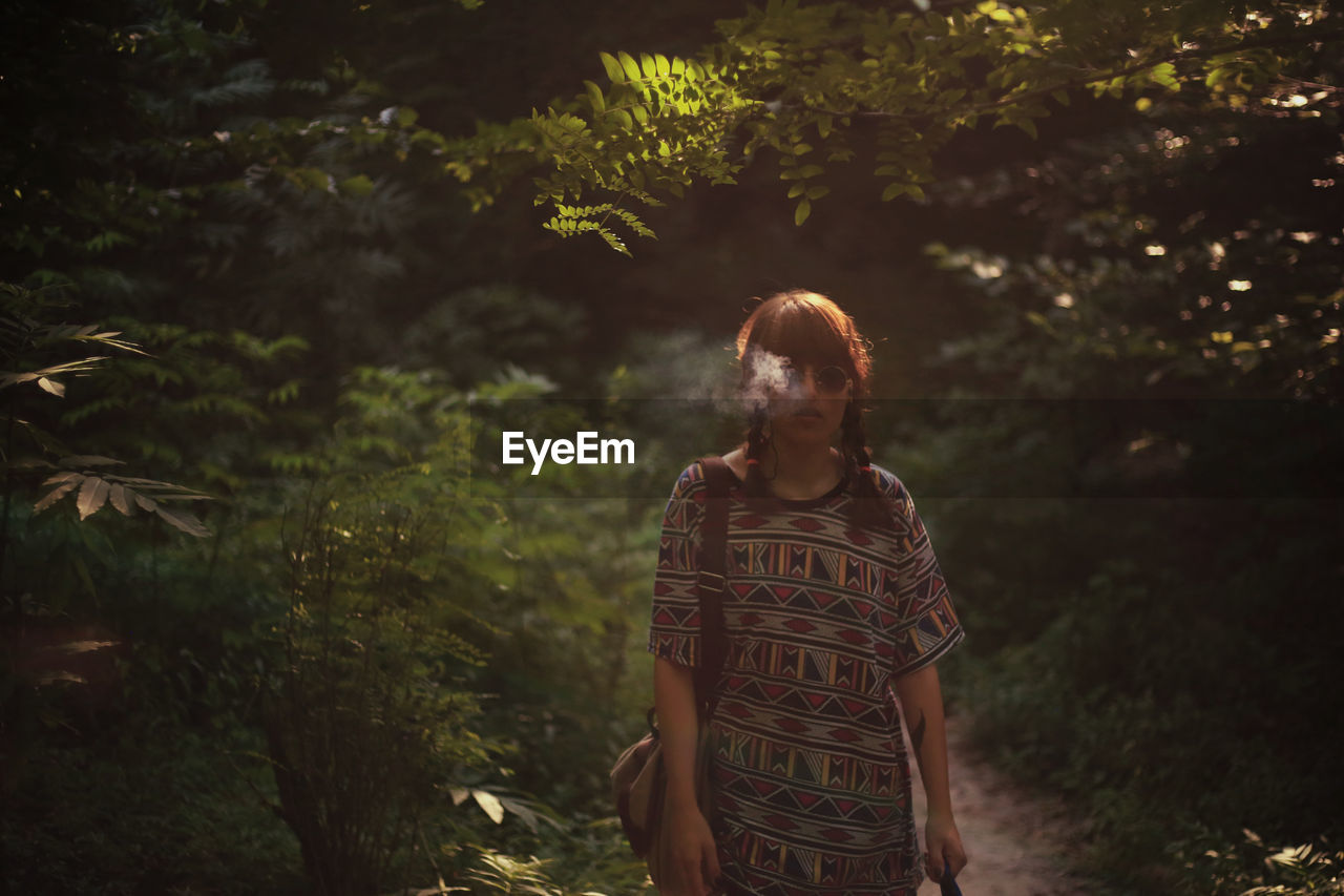 Young woman smoking while standing against trees in forest